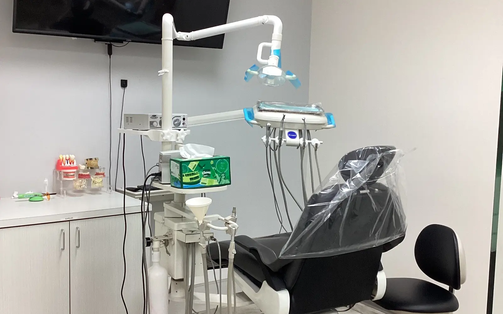 A treatment room at Diamond's Dental Inc. with a dental chair, overhead light, instrument tray and wall-mounted monitor